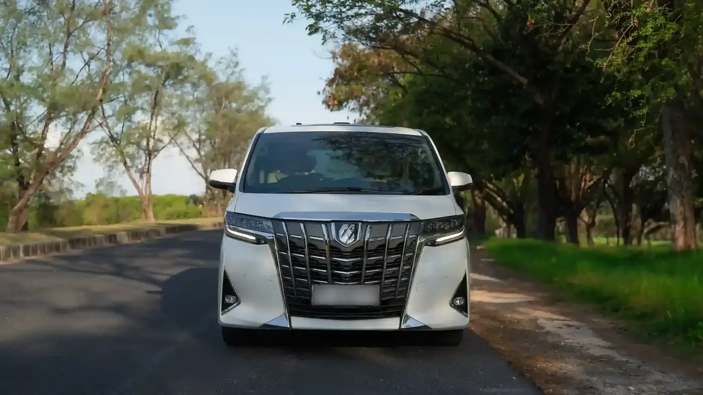White Toyota Alphard with private chauffeur on a tree-lined road in Bali